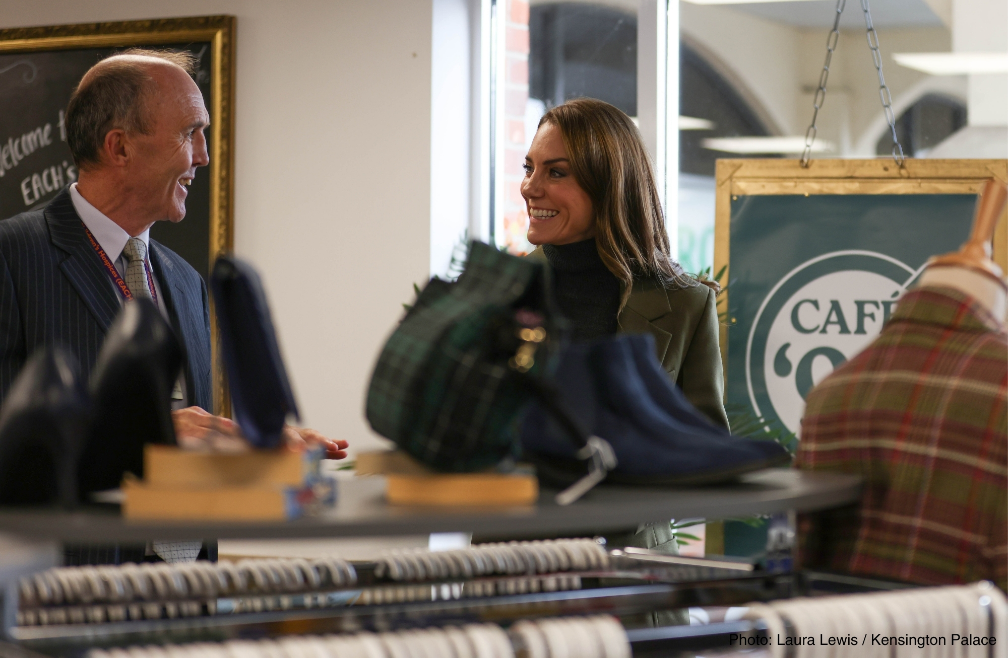 Kate Middleton and a member of staff standing beside a clothing rail in the EACH charity shop
