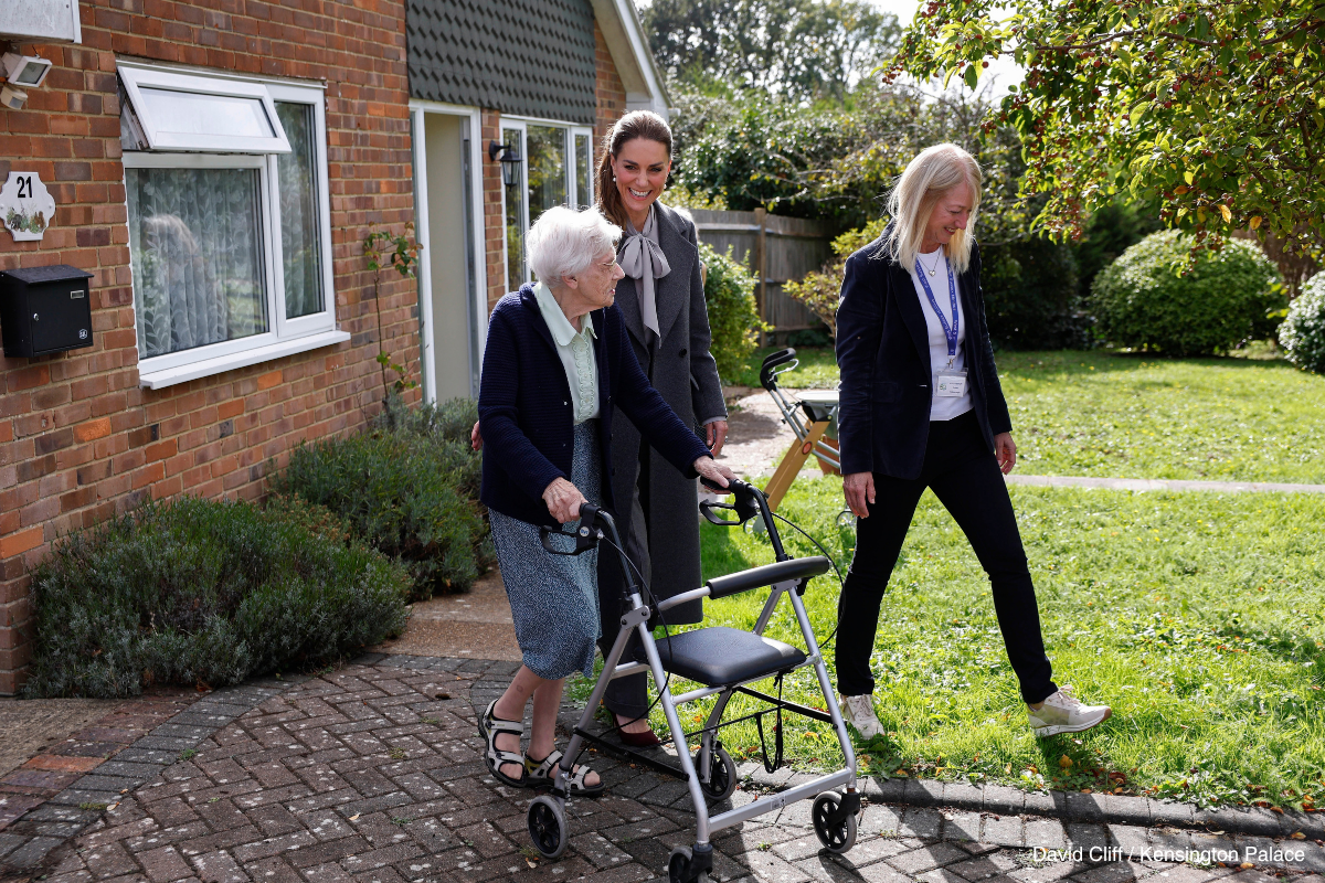 Kate Middleton walking beside a minibus passenger using a walking frame