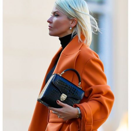 Model wearing an orange coat carries the black croc print Aspinal bag