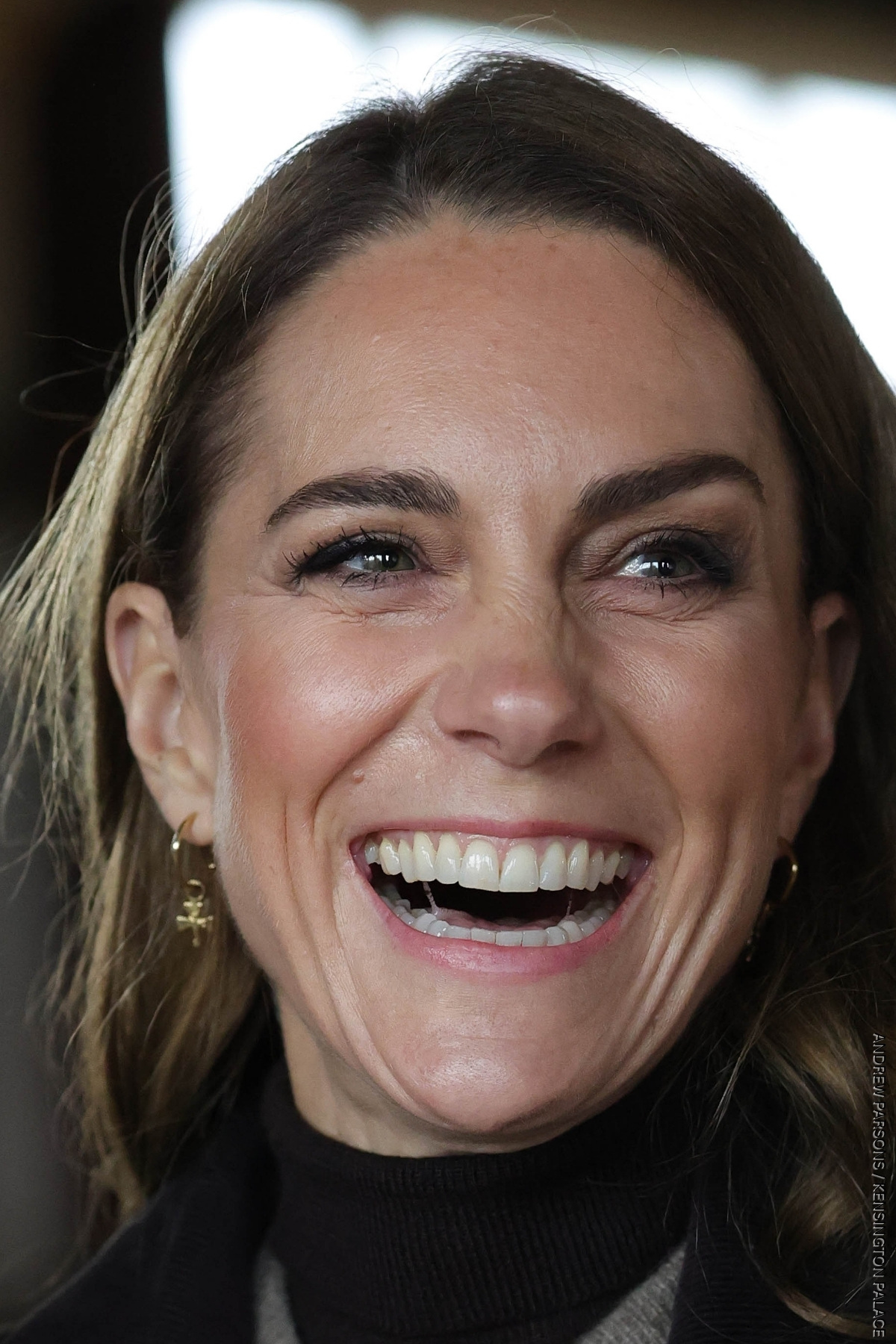 A super tight shot of Kate Middleton's face, she is laughing and looking to the side.

In her ears, are the Daniella Draper gold hoop earrings and Shamrock charms.