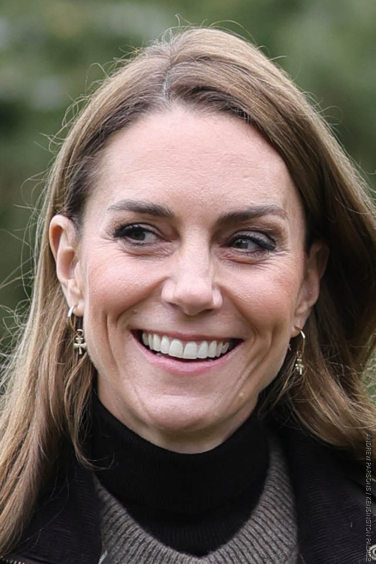 A close-up photograph of the Princess of Wales smiling, her gold hoop earrings with shamrock charms are visible