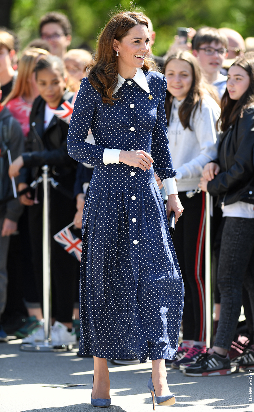 Kate smiles as she walks through a crowd, wearing a blue polka dot dress by Alessandra Rich