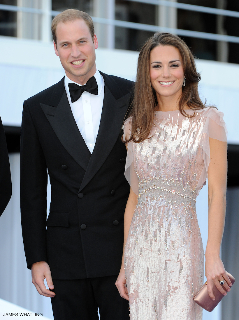 Kate Middleton stands smiling with Prince William as the pair pose for a photo at the 2011 Ark Gala.  The Princess faces the camera wearing the iconic pink dress by Jenny Packham.