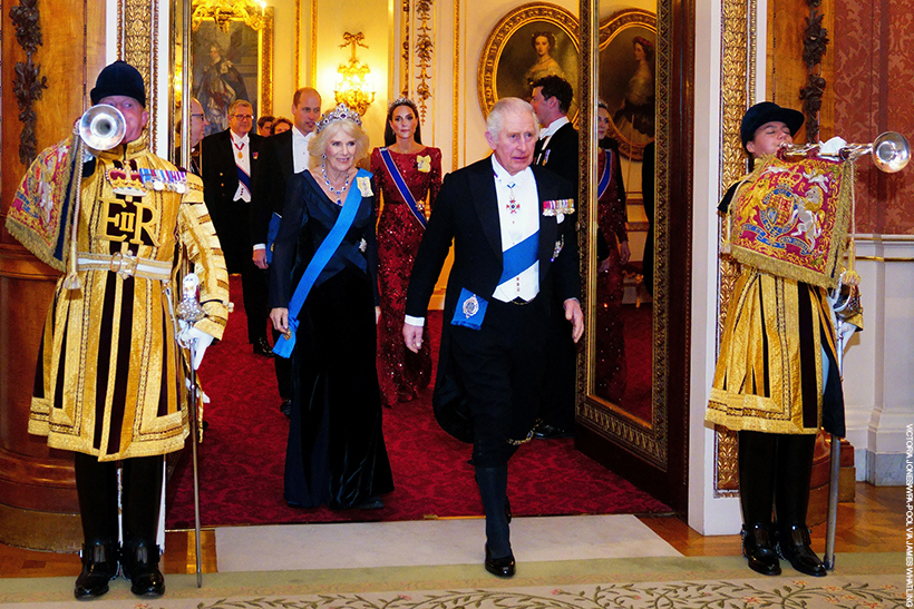 Royal guests arriving at the 2022 Diplomatic Reception. King Charles and Queen Camilla lead the procession through a set of doors as costumed trumpeters play.