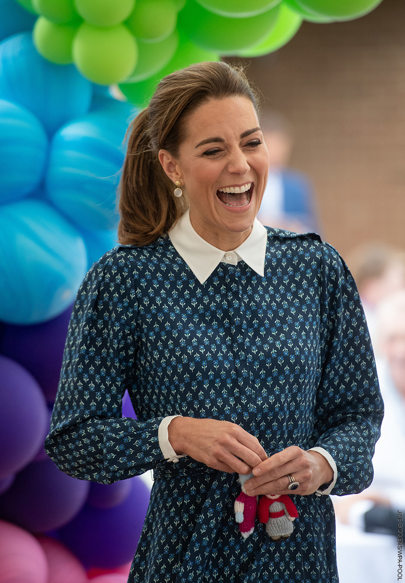 Kate Middleton wearing a stylish blue dress, stood in front of balloons, laughing