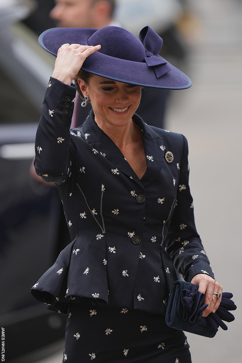 Kate Middleton holding on her navy bow hat as she battles the windy weather