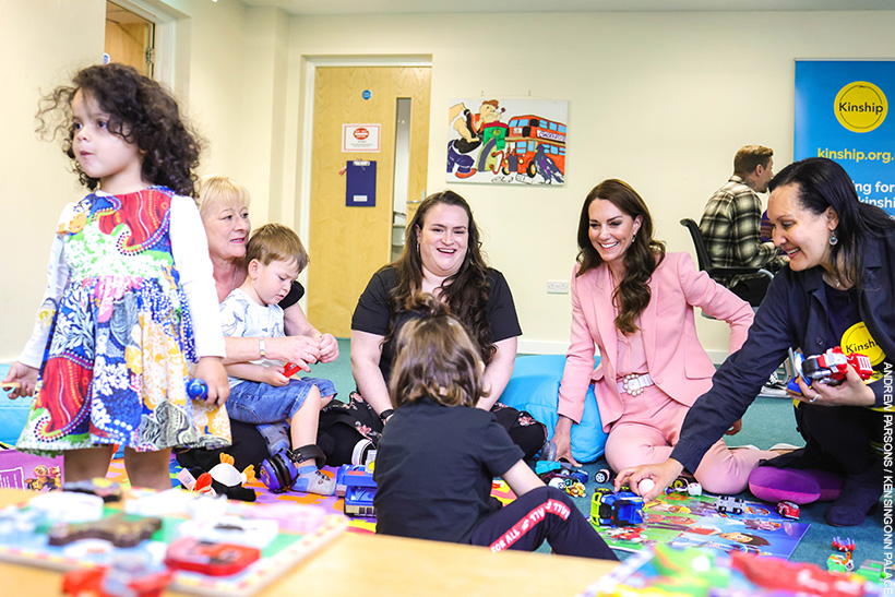 Kate Middleton playing with children at a Kinship support group.  She's wearing a pink suit with pearl accessories. 