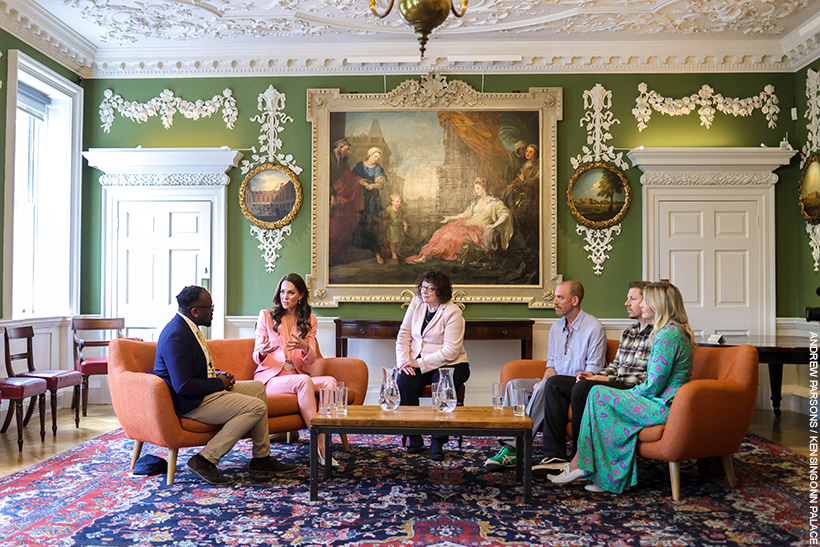 Kate Middleton chatting with people inside the Foundling Museum.  She's wearing a pink suit with pearl accessories. 