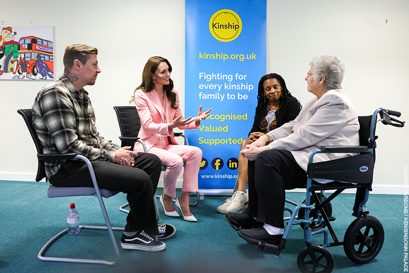 Kate Middleton chatting with people at a Kinship support group.  She's wearing a pink suit with pearl accessories. 