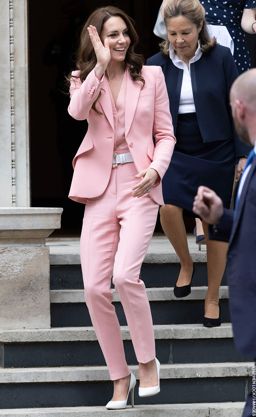 Kate Middleton waving as she leaves the Foundling Museum.  She's wearing a pink suit with pearl accessories and white heels.