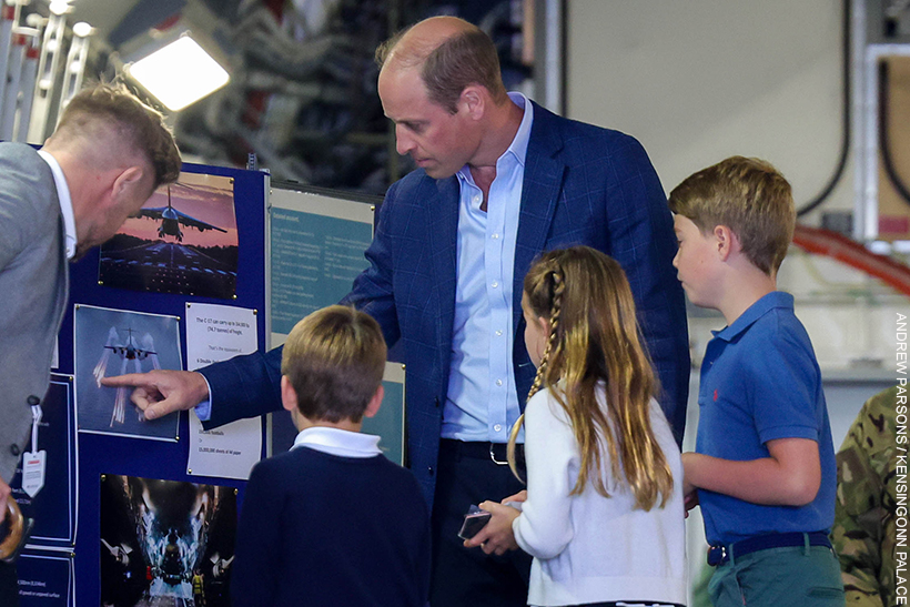 William, George, Charlotte and Louis look at a billboard with information about aircraft. 