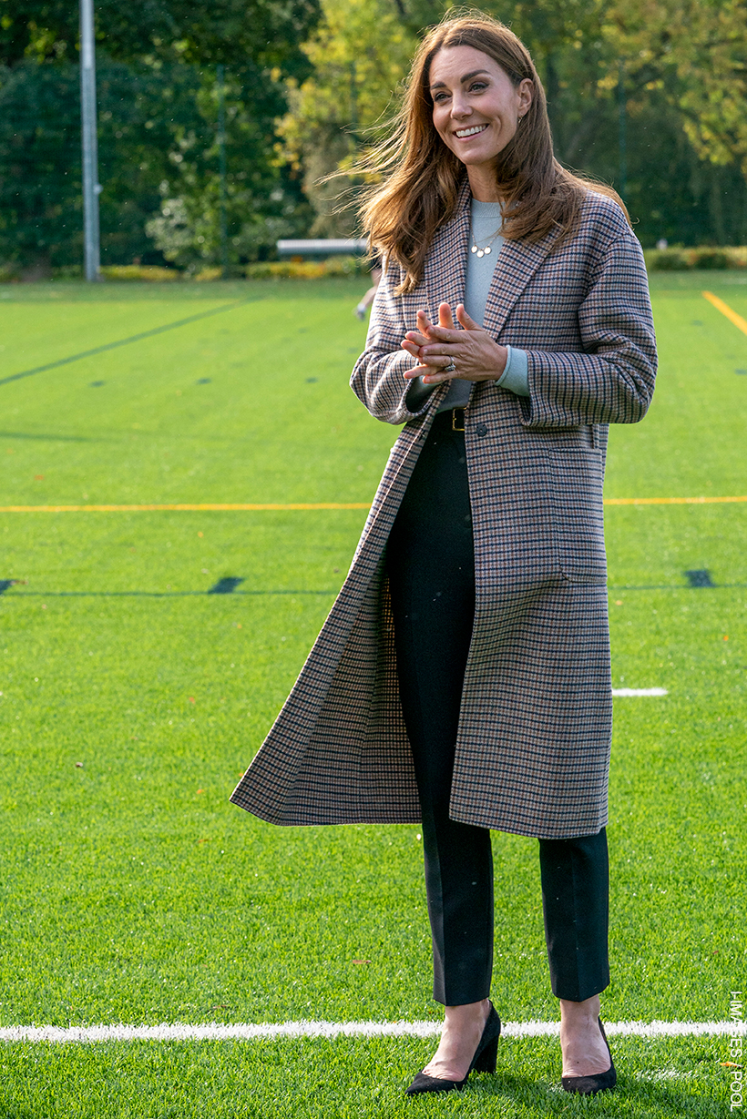 Kate Middleton wears a mid length check coat, blue sweater, smart trousers and heels while visiting a university. 