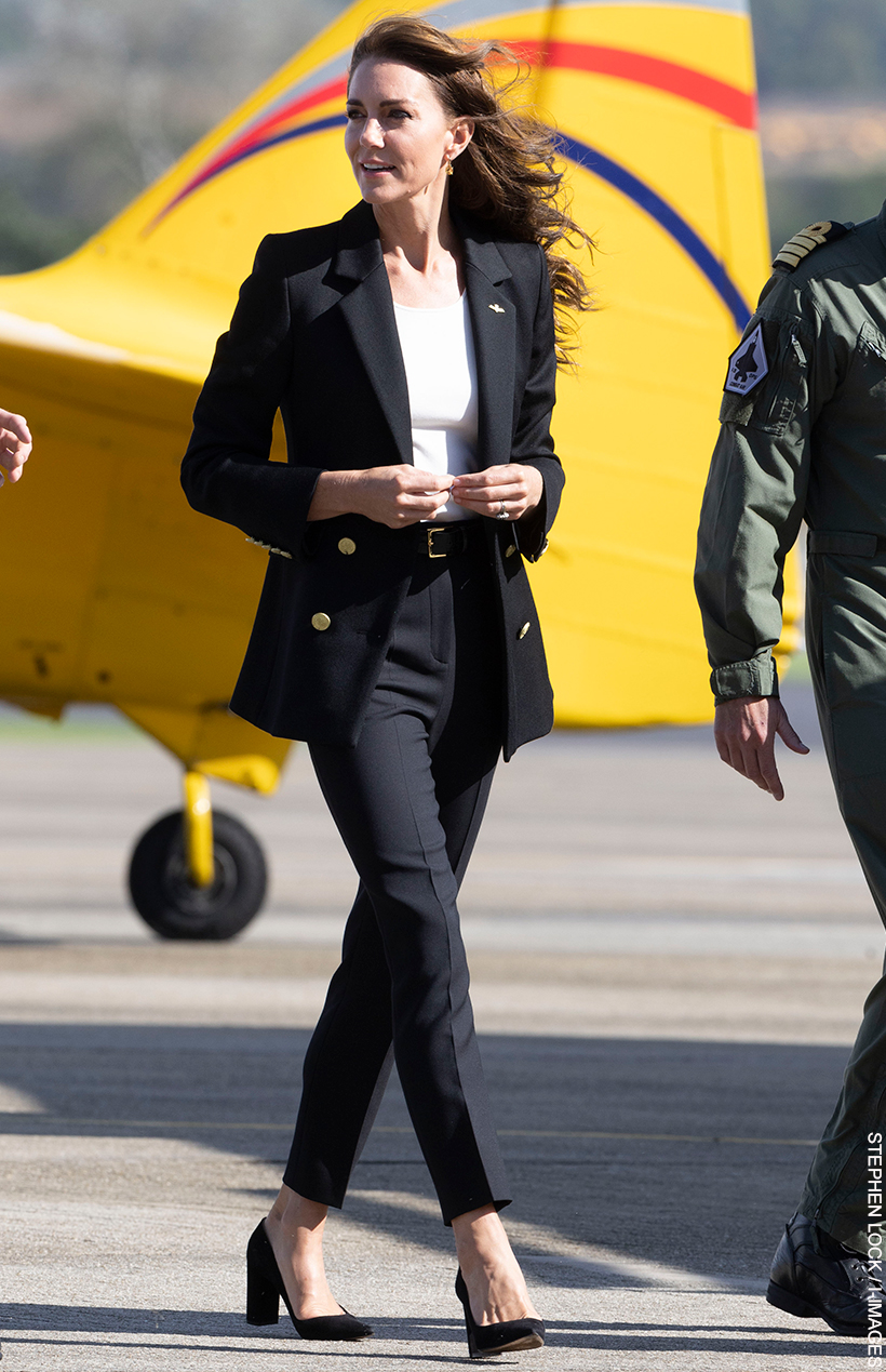 Kate Middleton visited RNAS Yeovilton wearing a black blazer, white t-shirt and black trousers.  She's walking with naval officers in front of a bright yellow plane, which contrasts with her black outfit. 