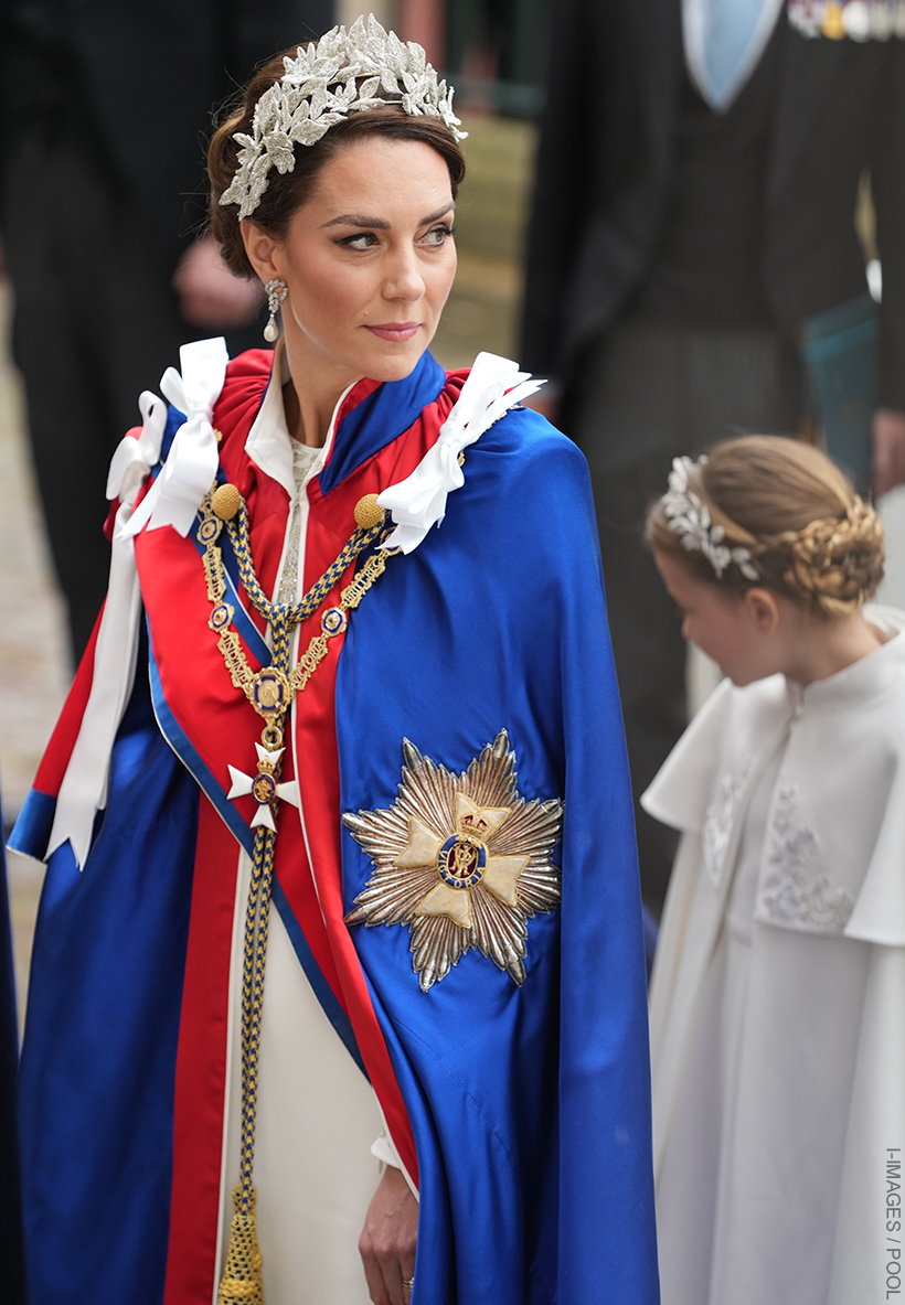 Kate Middleton wearing an Alexander McQueen headpiece and gown during the Coronation.  In the background, Princess Charlotte can be seen, also in McQueen headband and dress.