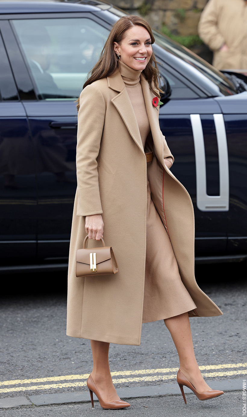 Kate Middleton, wearing a coat, skirt and top in matching camel tones, carrying the toffee coloured Demellier Nano Montreal bag.  She is walking away from a car. 