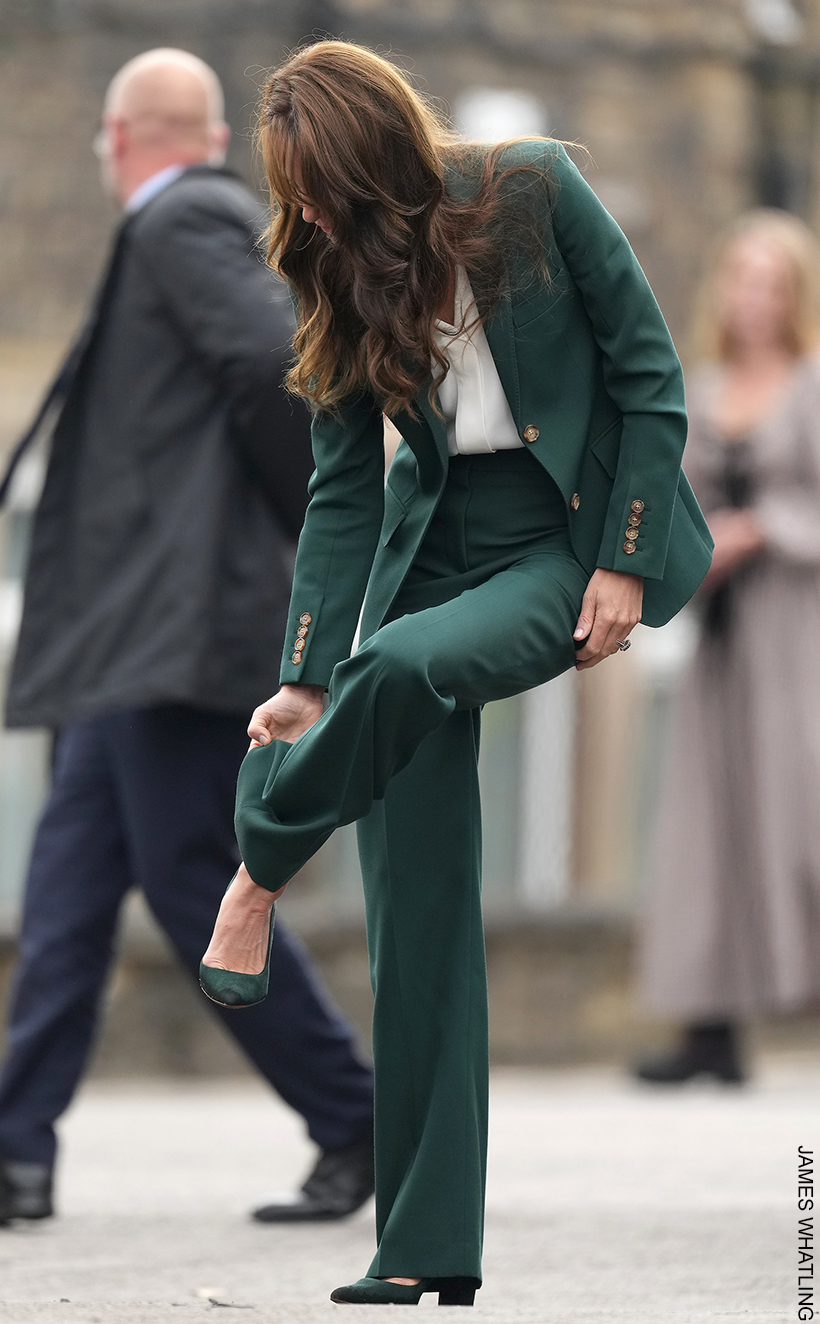 Kate Middleton lifting her leg up and pulling the hem of her green suit out of her Emmy London Josie pumps.  You can clearly see the block heeled shoe in the image.