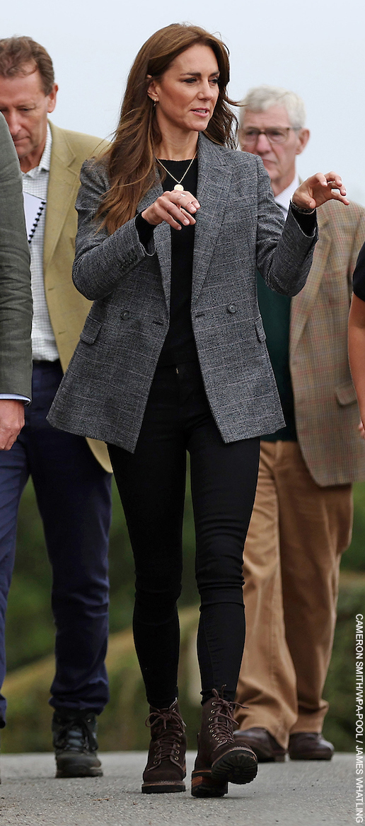 The Princess of Wales in Cornwall.  The Princess wears a grey check blazer, black sweater, gold necklace, gold earrings, black jeans and brown combat boots.