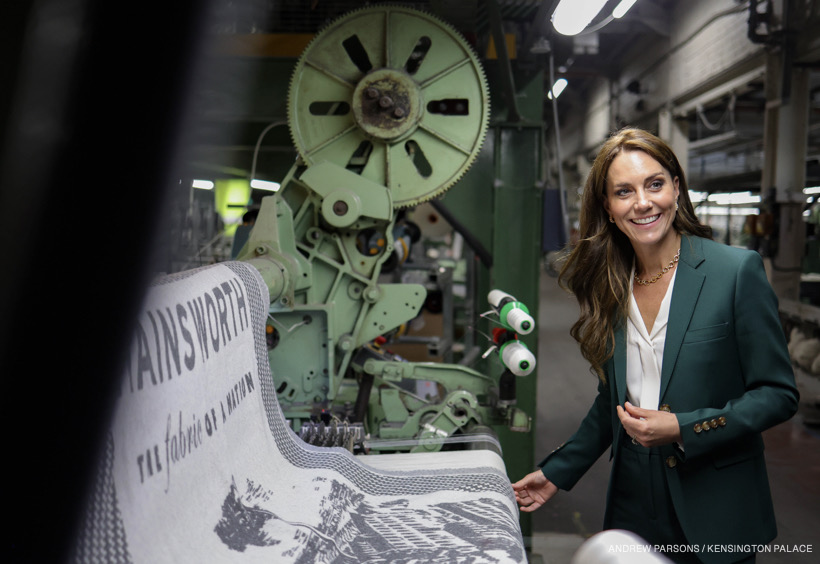 The Princess smiles as she touches a piece of cloth on a machine in the textile factory. 