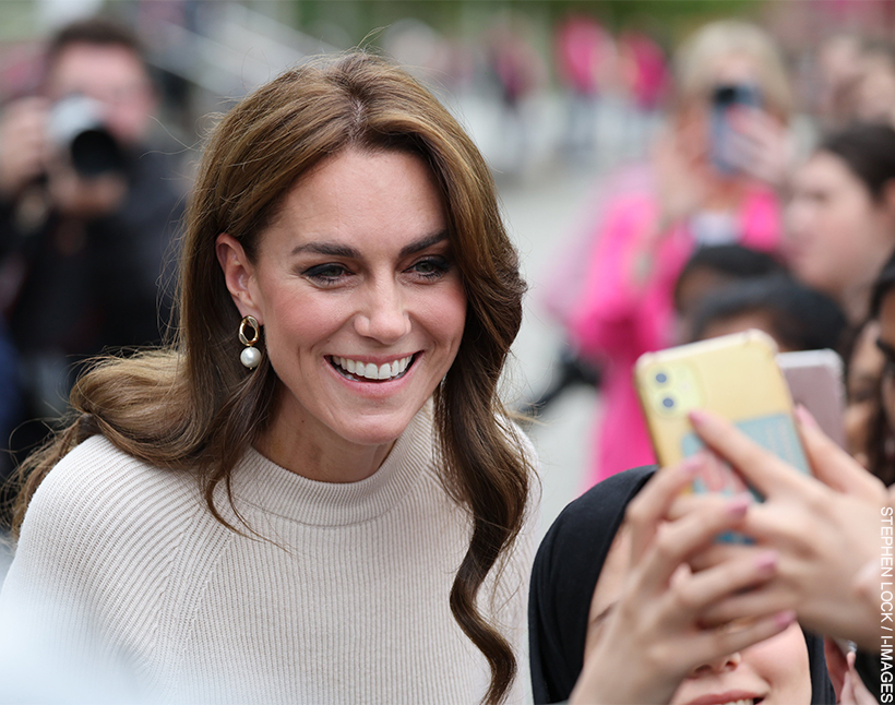 Kate Middleton, dressed in cream and wearing pearl earrings, smiles as she snaps a selfie with a student at Nottingham Trent University.