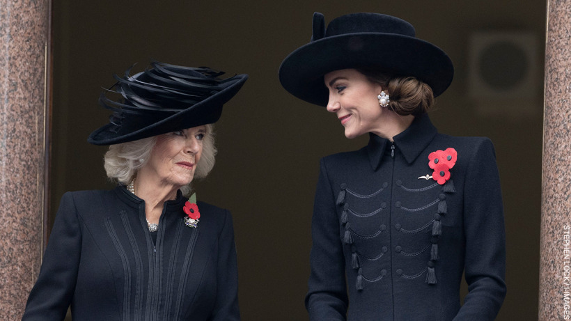 Kate Middleton and Queen Camilla on the balcony, both dressed in dark coats and wearing hats, sharing a moment of connection, with regal poise and elegance, on a day of national reflection.

