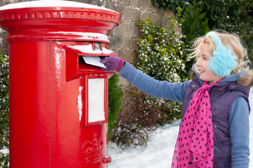 A little girl reaching into a red post box in the snow.
