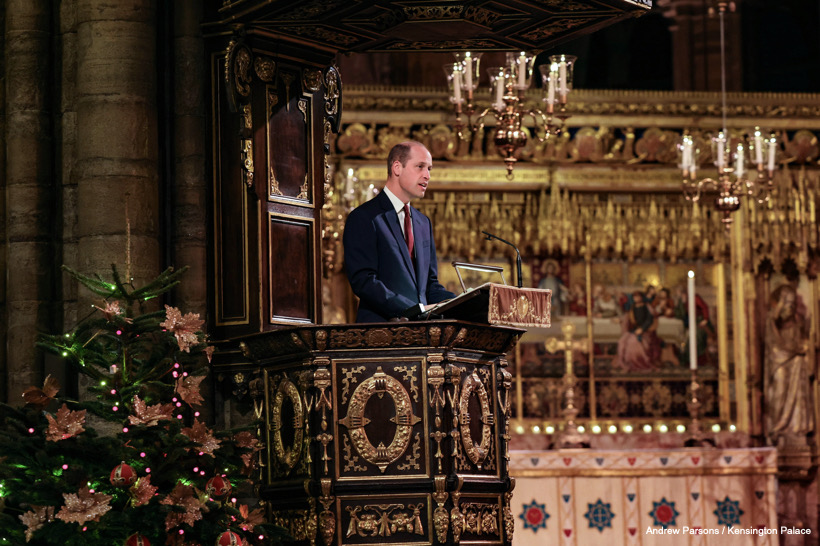The Prince of Wales speaks at a podium in front of a Christmas tree inside of Westminster Abbey.