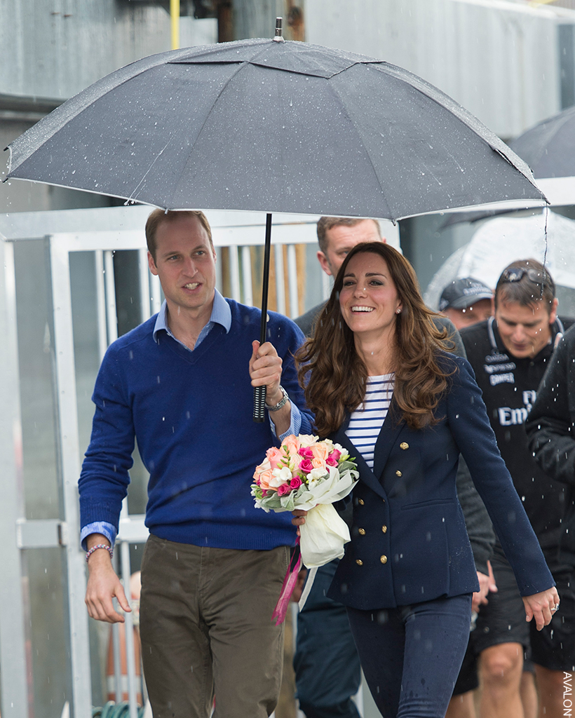 Prince William holds an umbrella over Kate as the rain pours. The pair are dressed in smart-casual attire.