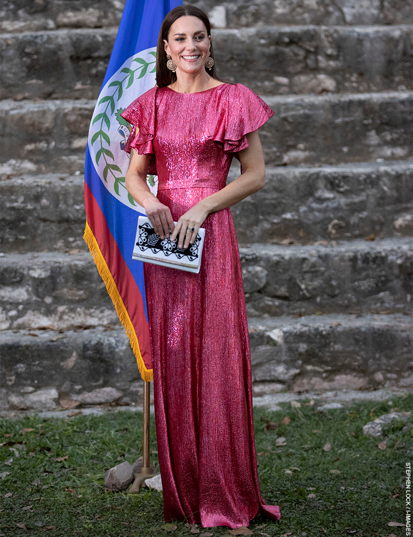 Kate Middleton wears a vibrant pink maxi dress with flutter sleeves in front of the Belize flag.