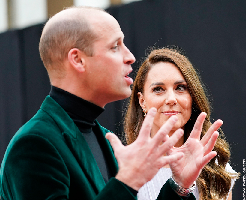 William, stood in a green jacket, is passionately expressing something to a person out of shot.  Kate looks on, smiling, with a look of pride in her eyes. 