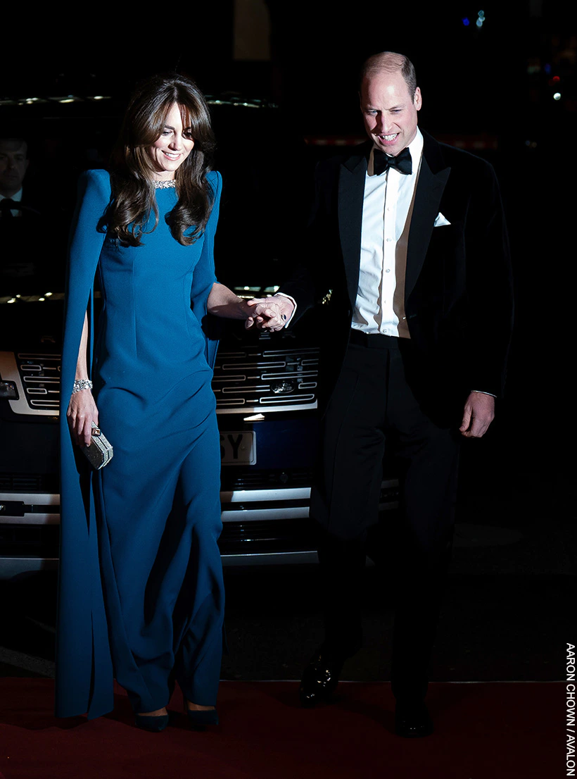 William and Kate hold hands as the prince helps his wife up the stairs of the Royal Albert Hall.  Both are dressed in formalwear. 