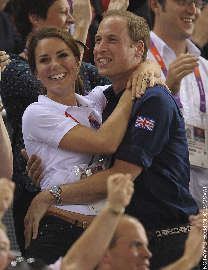 Prince William and Kate Middleton embracing.  Dressed in sporty polo shirts, the pair hug in celebration. Both smiling, Kate grabs William’s shoulders and he has his hands around her waist.  