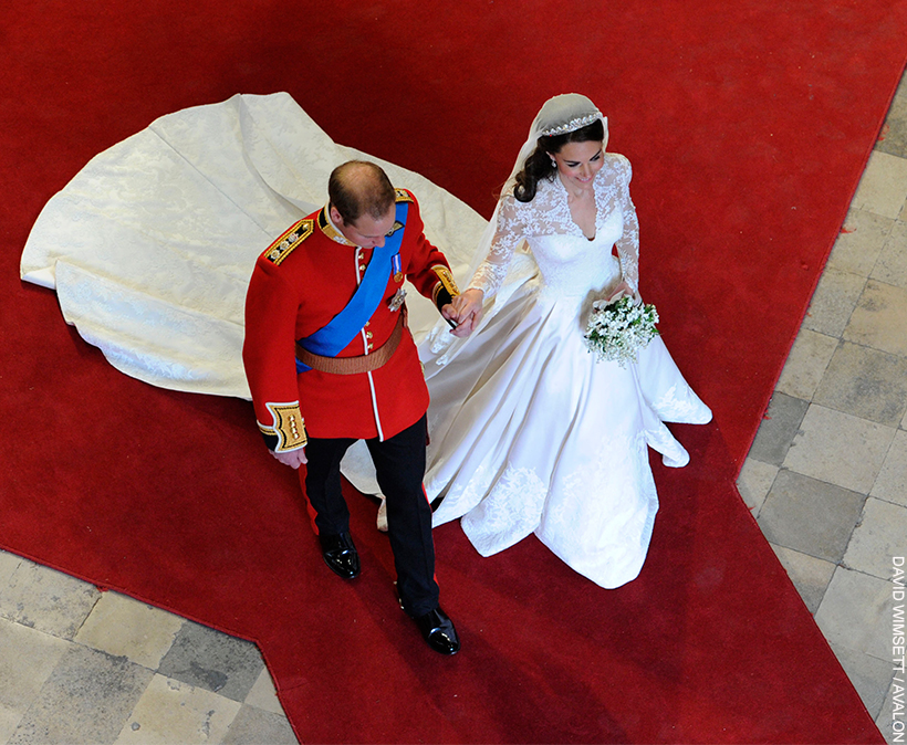 William and Kate walk hand in hand through Westminster Abbey, as husband and wife.  Both wearing wedding attire, Kate's dress train following behind. 