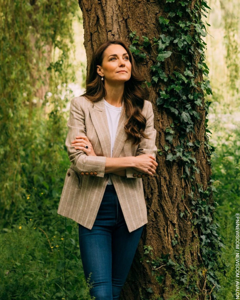 In this new photograph, The Princess of Wales stands with her back against a willow tree.  Her arms are folded.  She's wearing a beige pinstripe blazer with jeans.