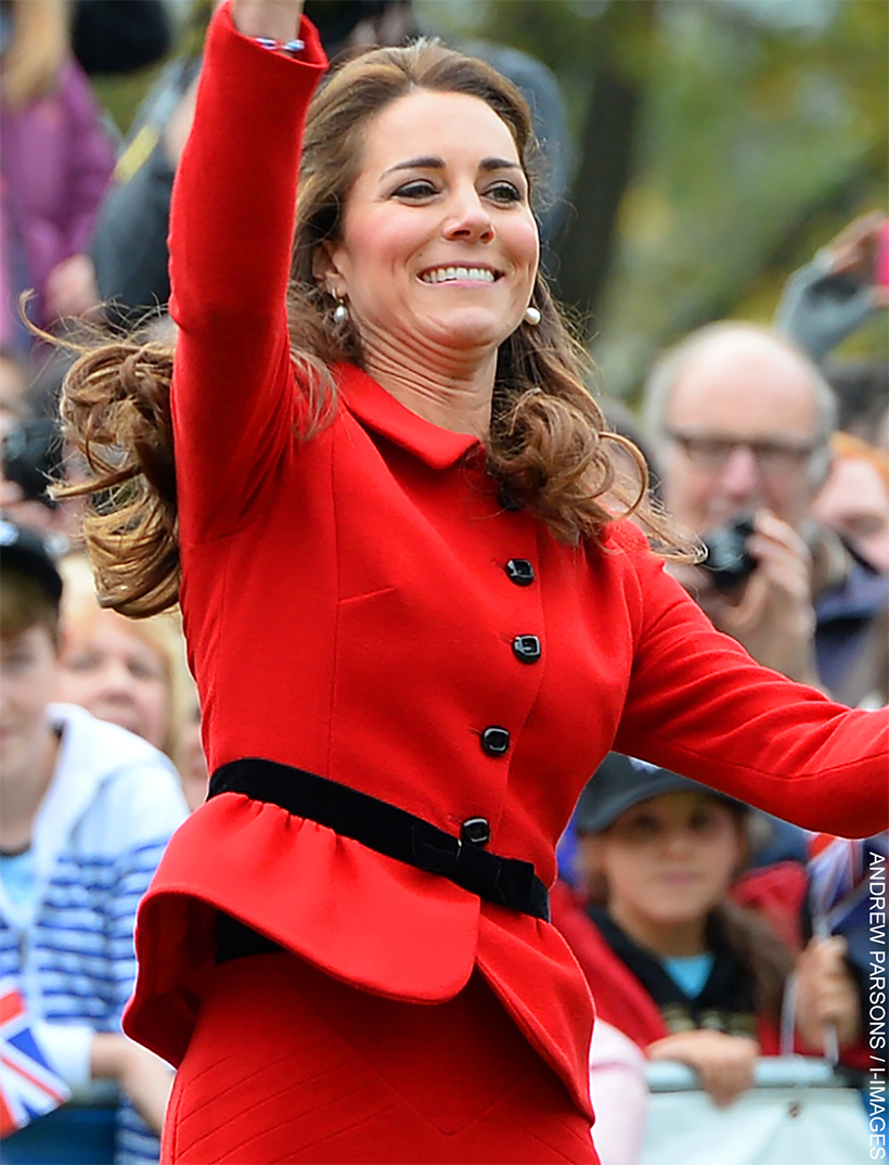 Kate Middleton wearing a vibrant red Luisa Spagnoli suit with a black belt and pearl earrings during her visit to Christchurch.  she is attempting to catch a cricket ball.
