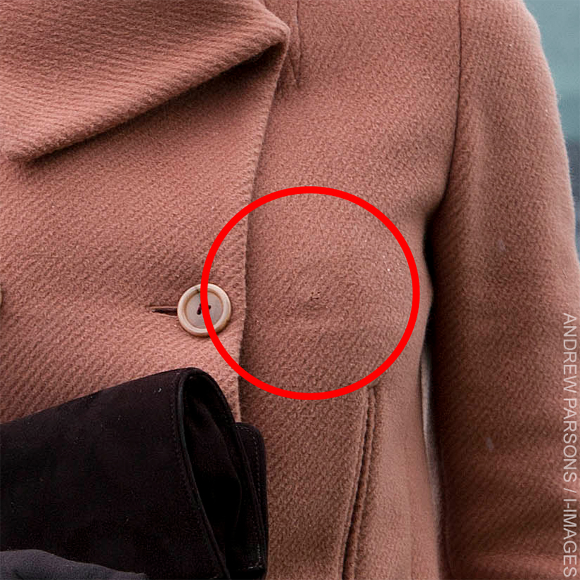 Close-up of Kate Middleton's salmon-coloured Joseph coat worn during the Cheltenham Festival in 2013, showing noticeable indentations on the fabric where buttons were repositioned to accommodate her changing figure at five months pregnant with Prince George.