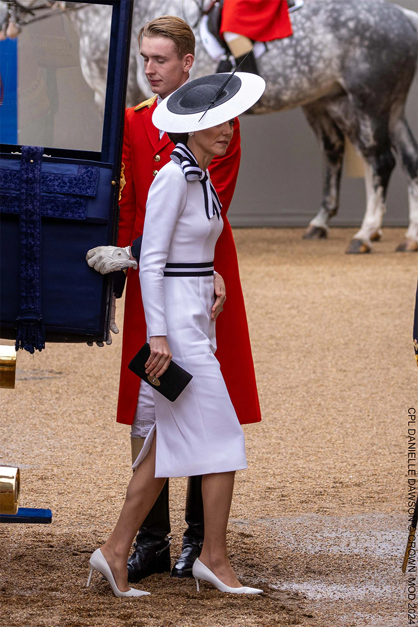 Kate steps out of the carriage wearing a white dress with black trim and matching hat. 
