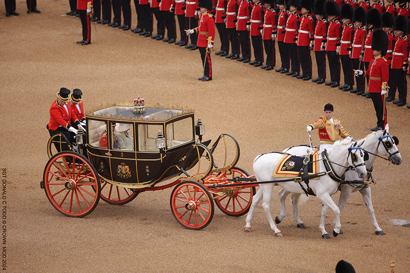 The gold Scottish State Coach being pulled by horse, with the King and Queen inside