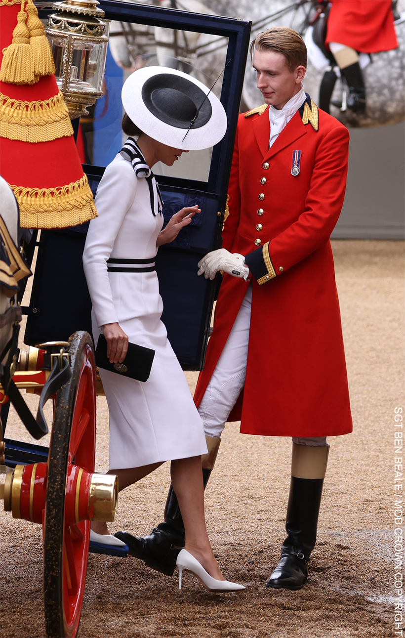 Kate steps out of the carriage wearing a white dress with black trim and matching hat. 