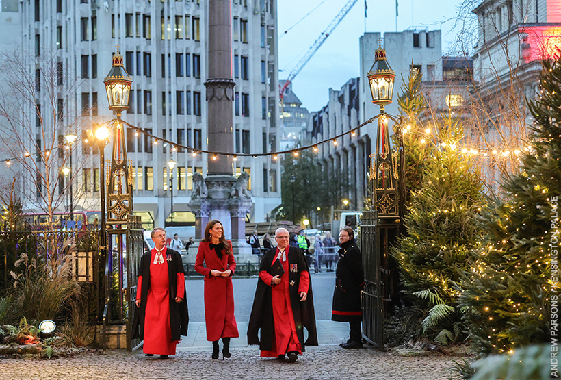 Kate Middleton wears a long red coat with a black velvet bow as she waves and walks into the 'Together At Christmas' Carol Service being held at Westminster Abbey.  She walks with two clergymen. 