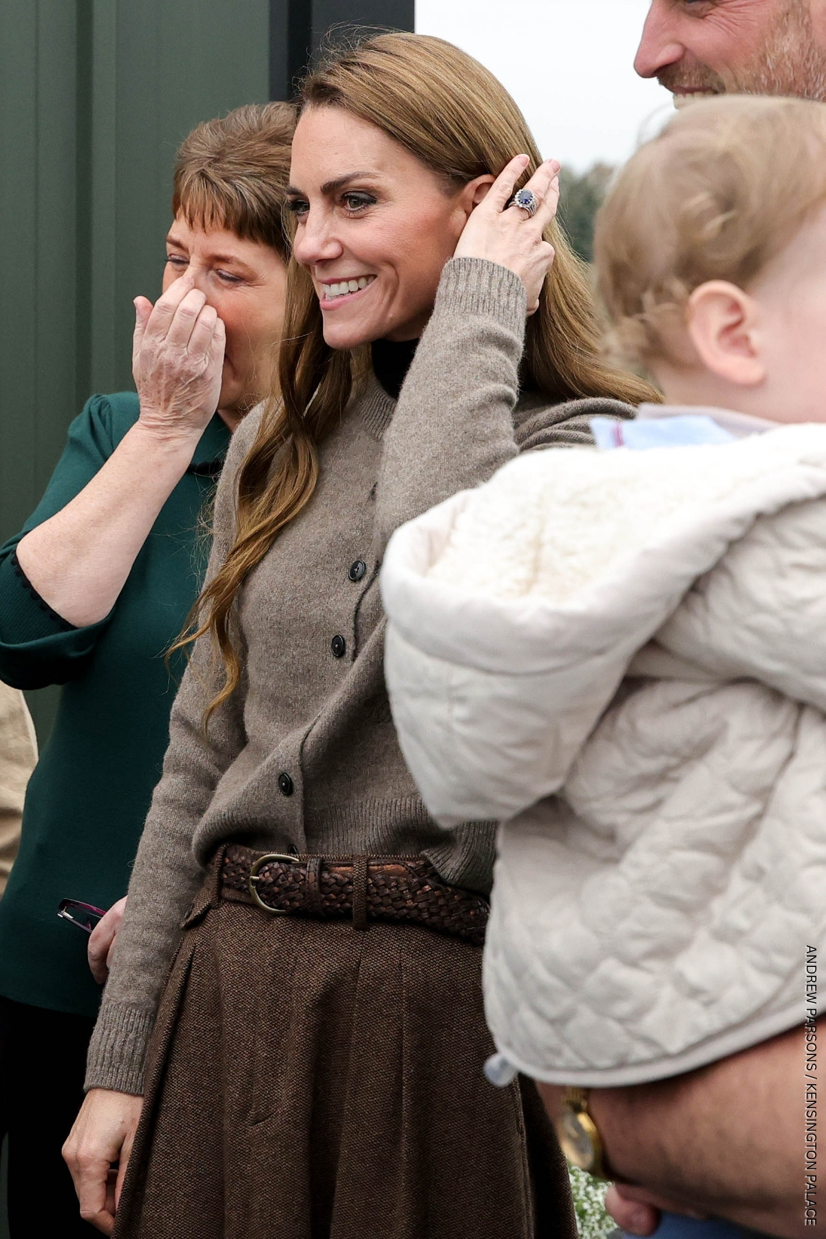 The Princess of Wales smiling and chatting with the family at the farm, wearing the brown yak's wool cardigan from WNU
