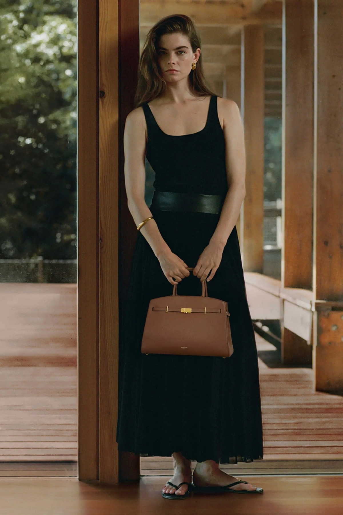Model wearing black dress, carrying the DeMellier Midi Hudson in tan leather.