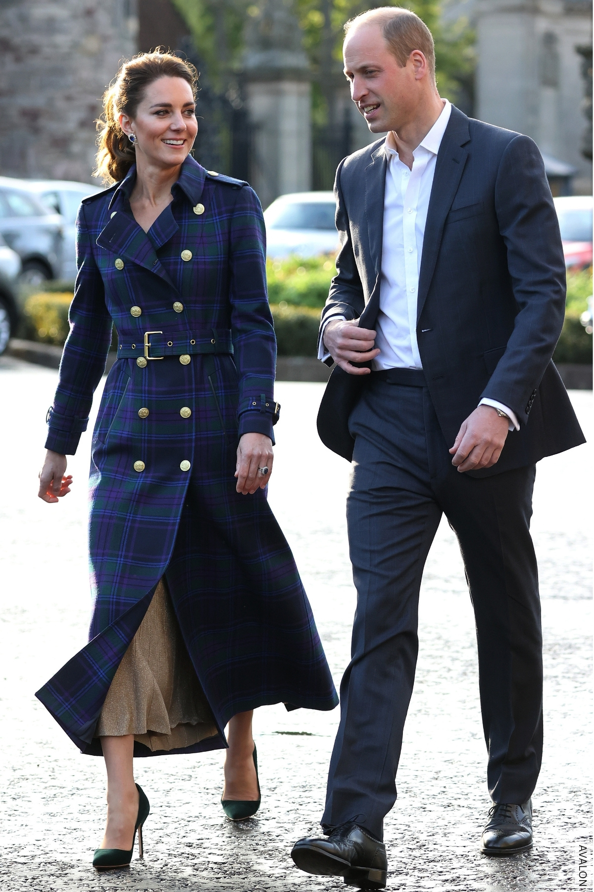 The Prince and Princess of Wales walk together outside. Kate wears a checked trench coat. 