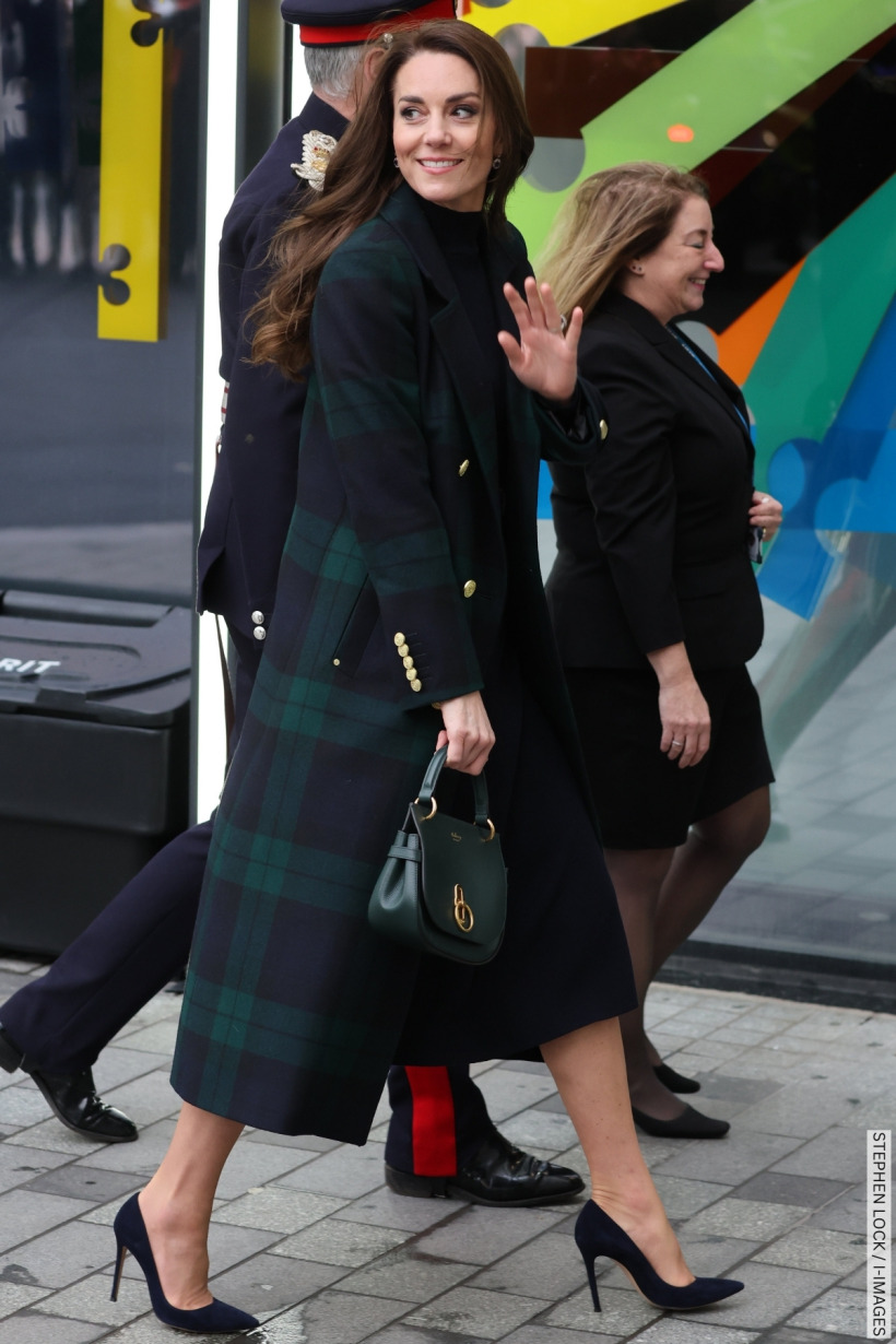 The Princess of Wales walks into a building wearing a green and blue tartan coat, carrying a green handbag. 