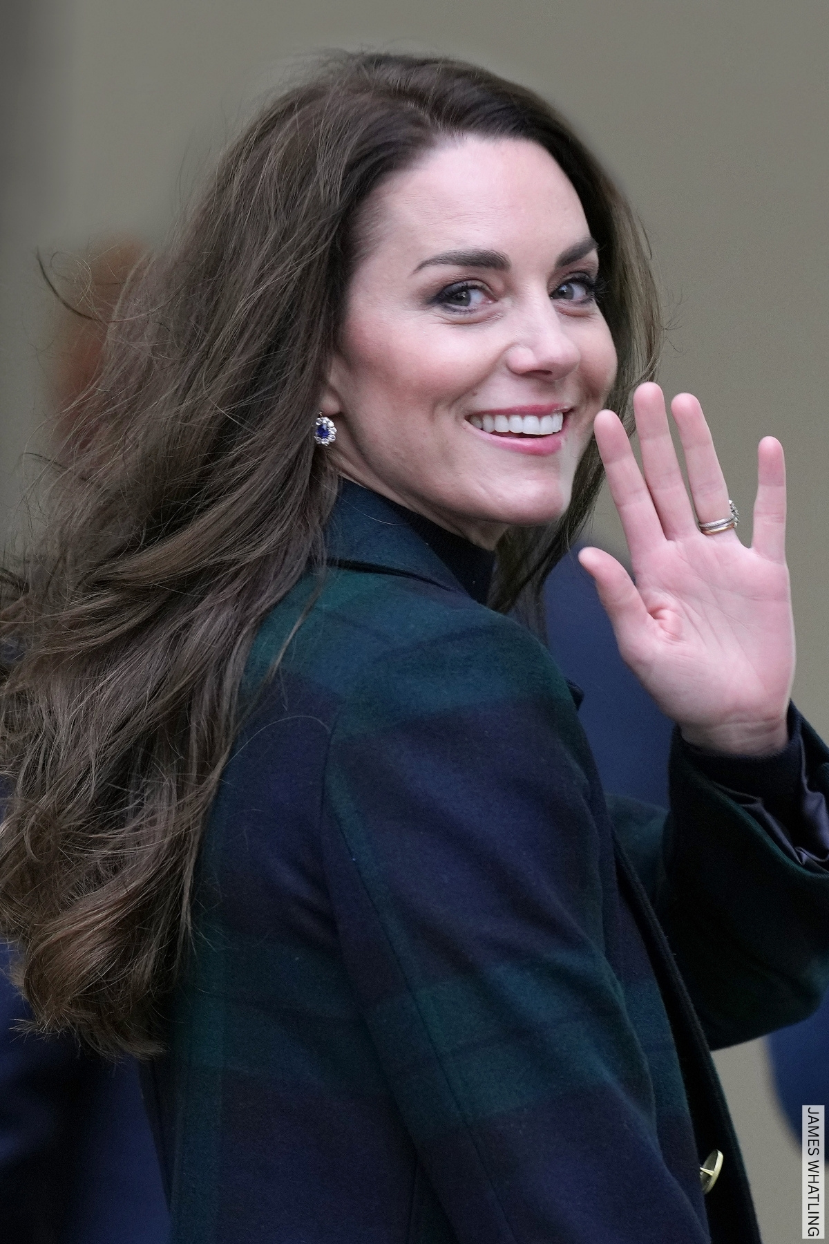 Kate Middleton turning to camera and waving. The Princess wears a blue and green checked coat.