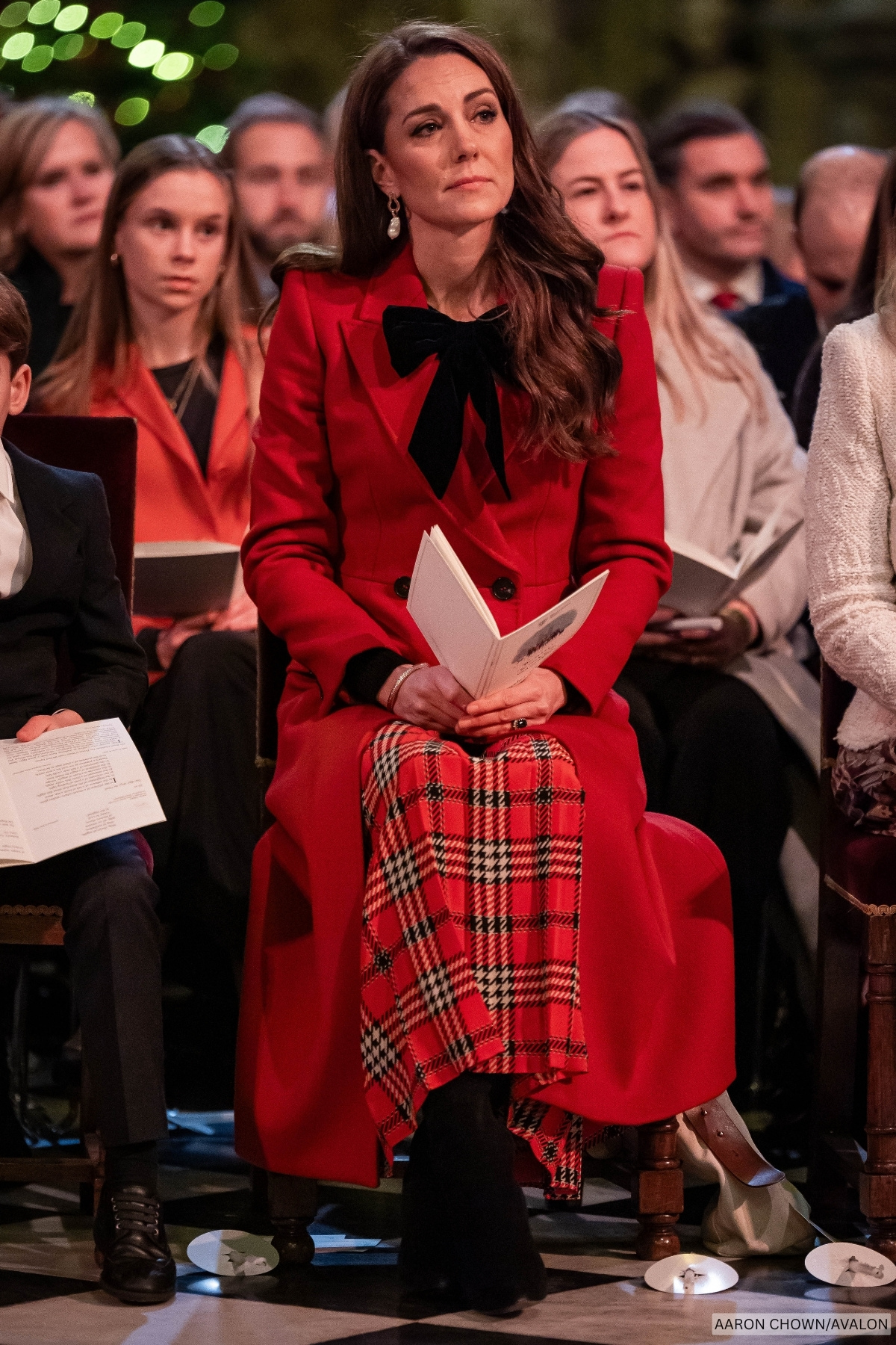 The Princess of Wales at her Christmas carol service wearing a red tartan skirt, long red coat and no detail at the neckline