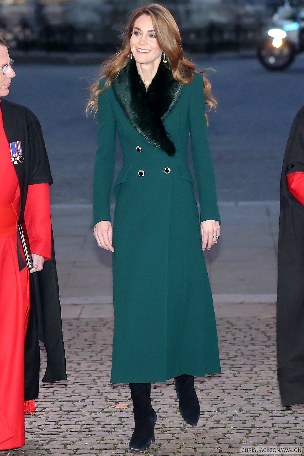 Full look at the Princess of Wales's outfit for the 2025 Together At Christmas carol concert. The princess wears a deep green wool coat topped with a green faux fur lapel, and dangling star earrings.