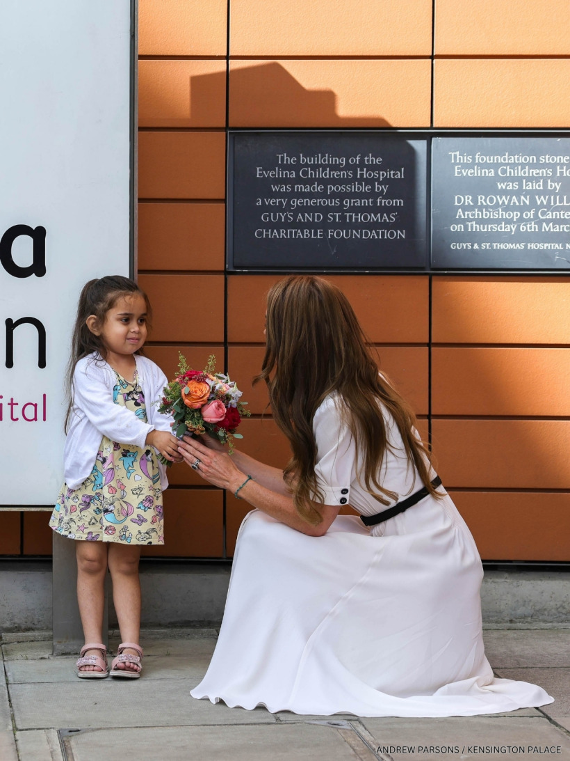 Kate Middleton wearing her white Suzannah 'Flippy Wiggle' dress during the Evelina London visit, as she receives flowers from a young girl