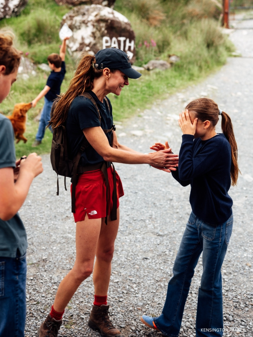 Kate Middleton in a navy top and red North Face shorts chatting to Princess Charlotte after the walk